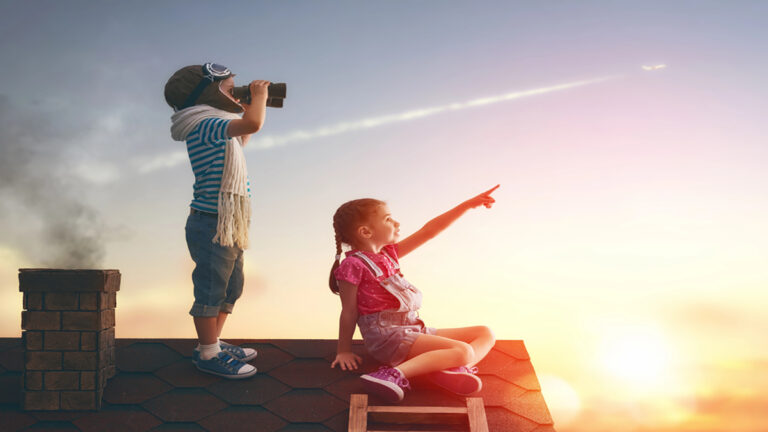 Girl on a rooftop pointing toward the sunset while a boy looks through binoculars nearby at dusk/Golden hour.