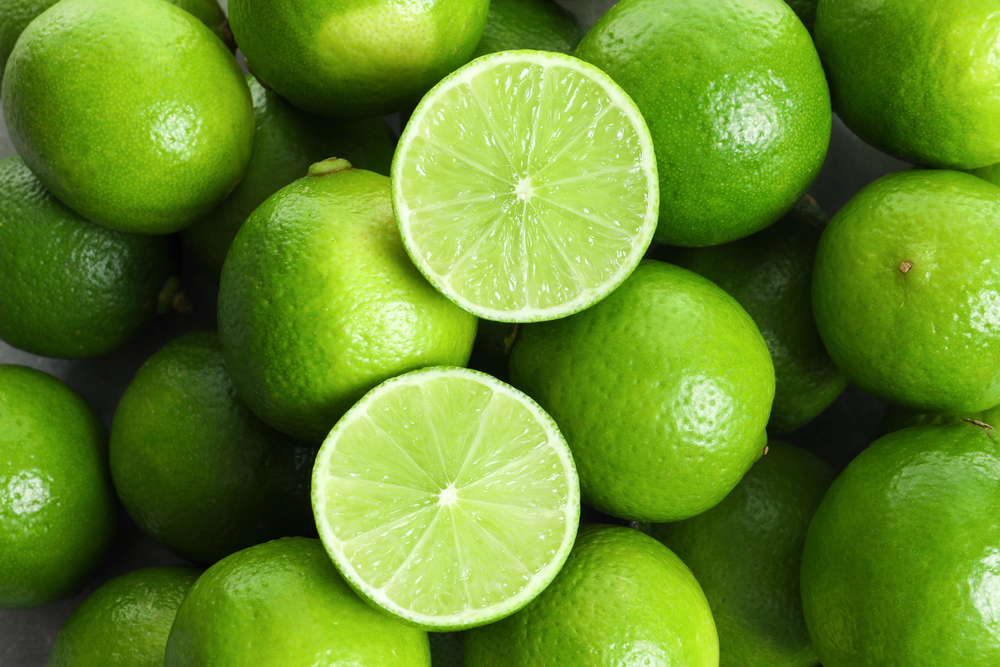 Pile of bright green limes with two halves showing juicy pale-green flesh in the center