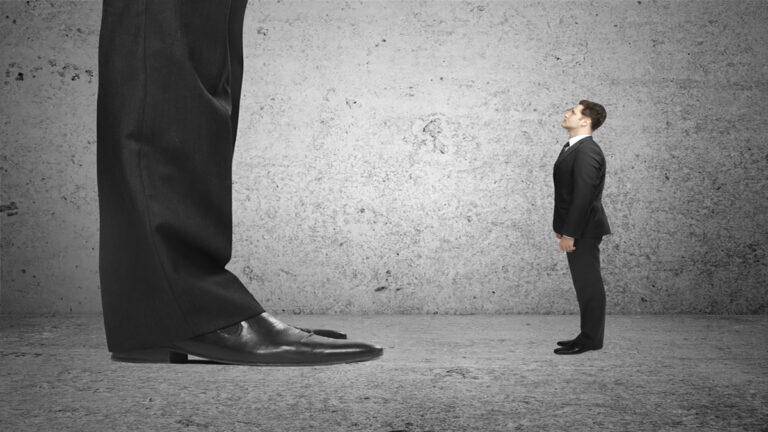 small businessman - Renuevo De Plenitud A gigantic man in a suit looms over a much smaller man in a suit, both standing on a concrete floor.