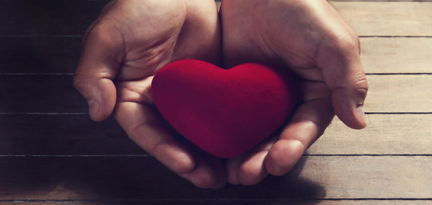 Hands cupping a red heart on a wooden surface, conveying care and compassion.