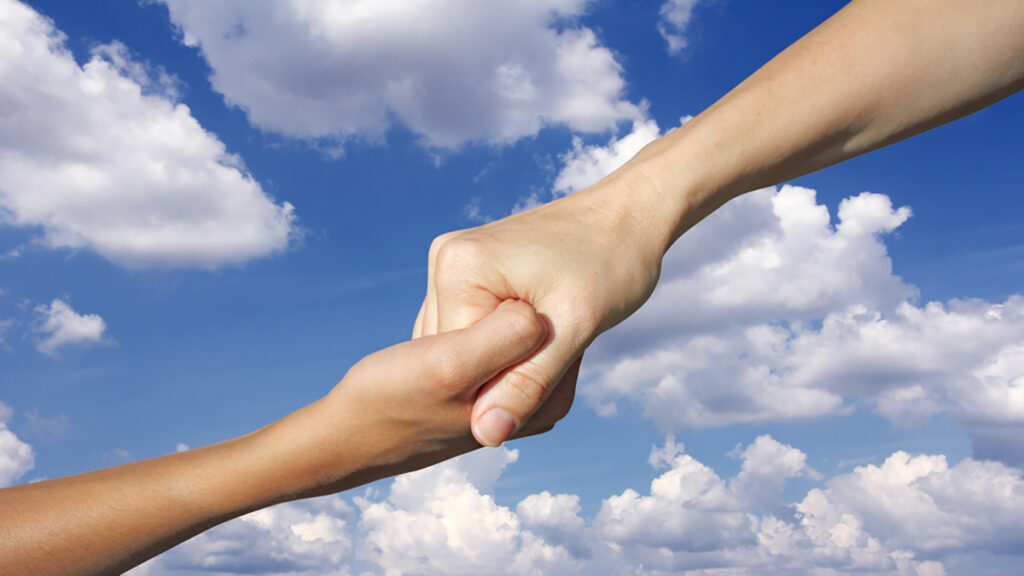 Two hands clasped in a firm grip against a blue sky with clouds, conveying support or teamwork.