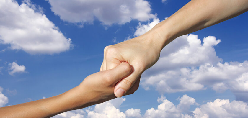 Two hands clasped in a firm grip against a blue sky with clouds, conveying support or teamwork.