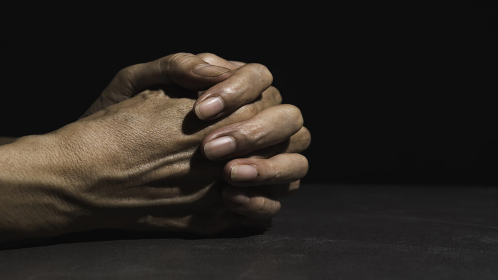 Two hands clasped together on a dark surface, fingers interlaced in a contemplative pose
