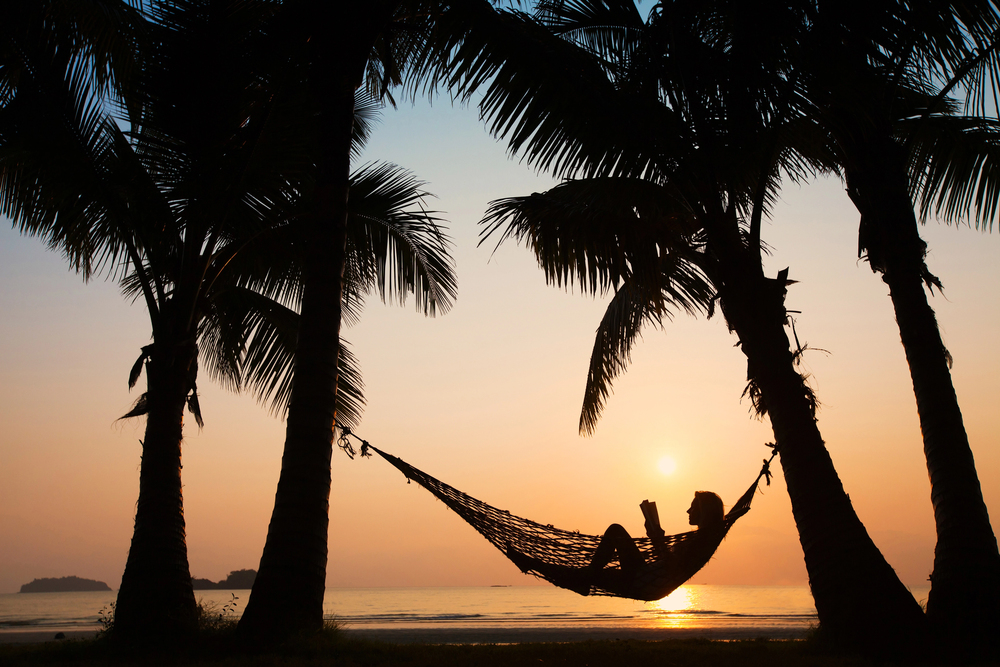 Depositphotos_32645249_S - Renuevo De Plenitud Person relaxing in a hammock between palm trees at sunset on a beach.