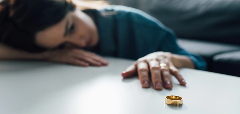 A person lies on a table nearby a gold wedding ring, suggesting loss or heartbreak.