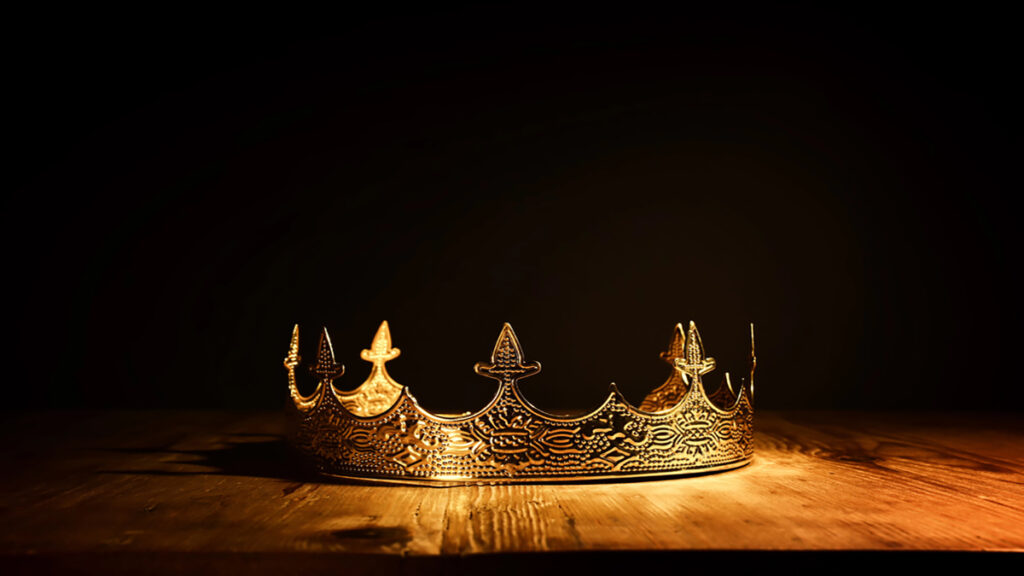 Ornate gold crown resting on a wooden table under warm spotlight with a dark background
