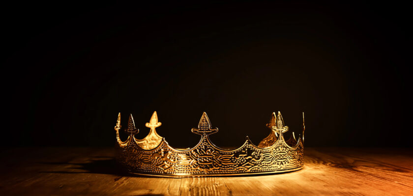 Ornate gold crown resting on a wooden table under warm spotlight with a dark background