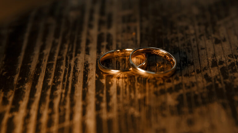 Two wedding bands placed on a dark, textured wooden surface with a warm glow and subtle engraving visible inside the rings.