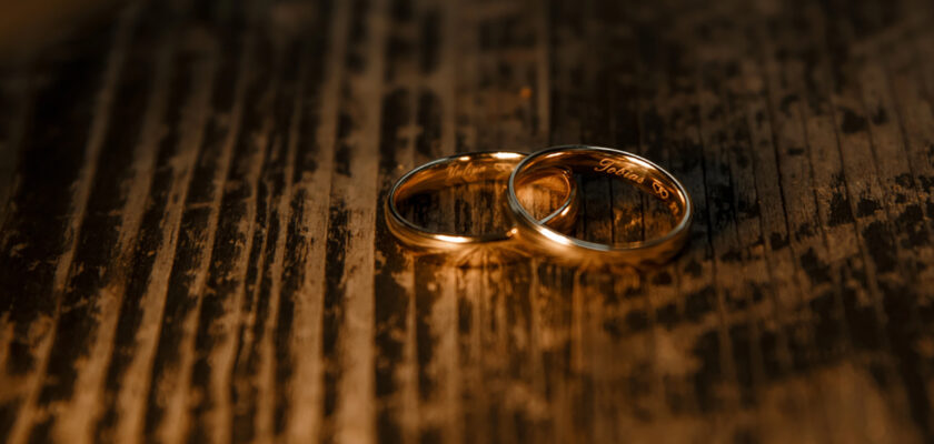 Two wedding bands placed on a dark, textured wooden surface with a warm glow and subtle engraving visible inside the rings.