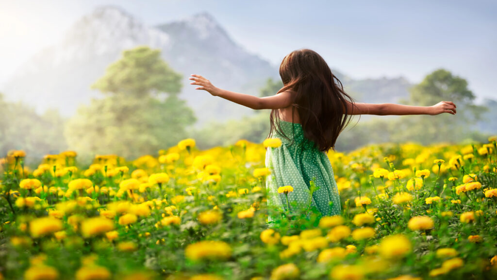 Girl in a green polka-dot dress spins with arms outstretched in a field of yellow flowers, mountains in the background (joyful freedom).