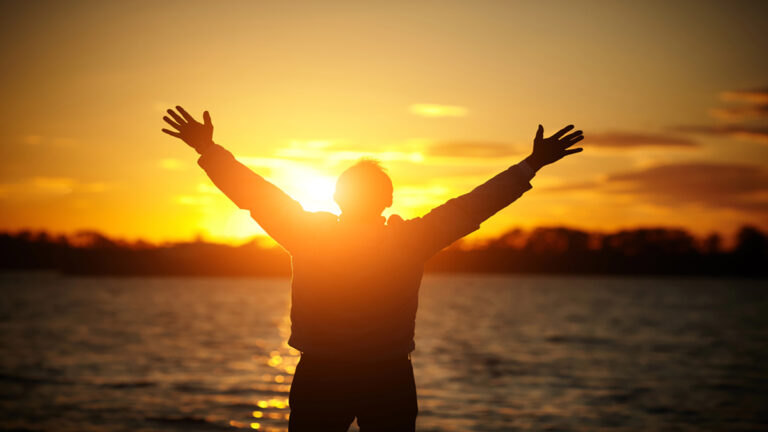 freedom - RDP dev Person silhouetted with arms raised at the shore during a golden sunset over a calm lake/twater.