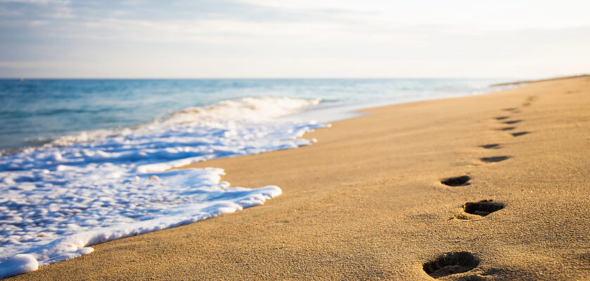 Footprints in wet sand along a shoreline with gentle waves at the water's edge.