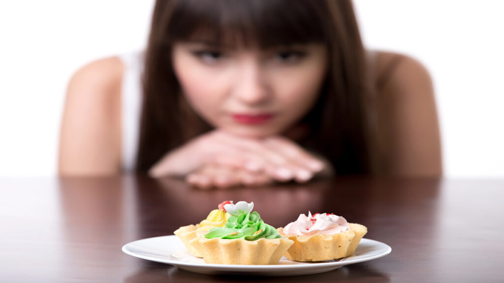 Two decorated mini tarts on a white plate with a blurred woman watching from the background.