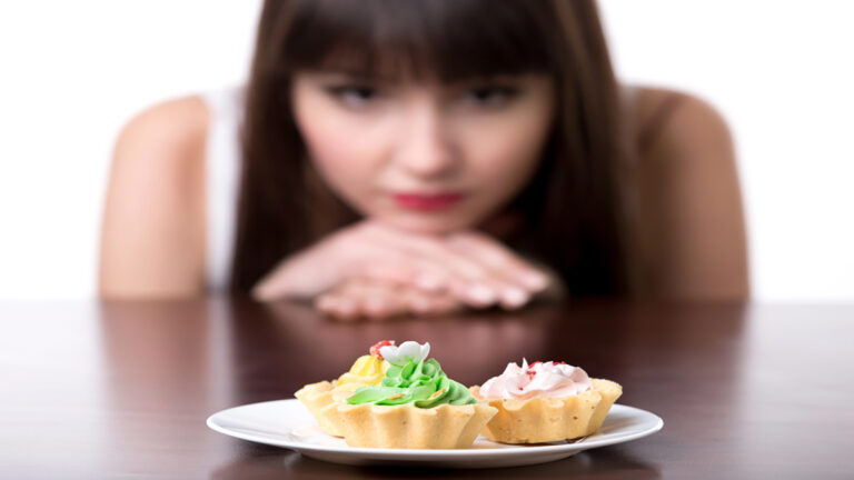 Two decorated mini tarts on a white plate with a blurred woman watching from the background.